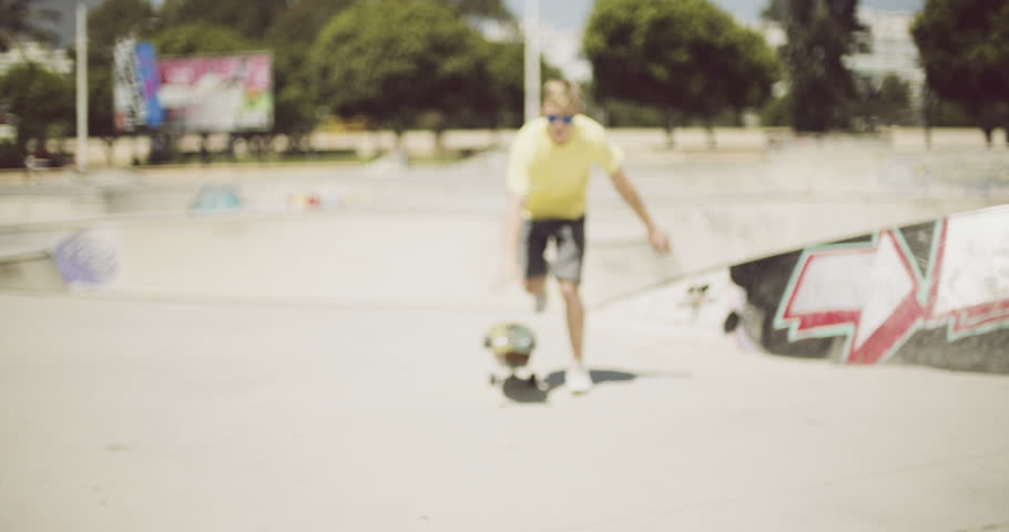 Young man enjoying a summer day skateboarding at the skate park launching himself towards the camera on his longboard