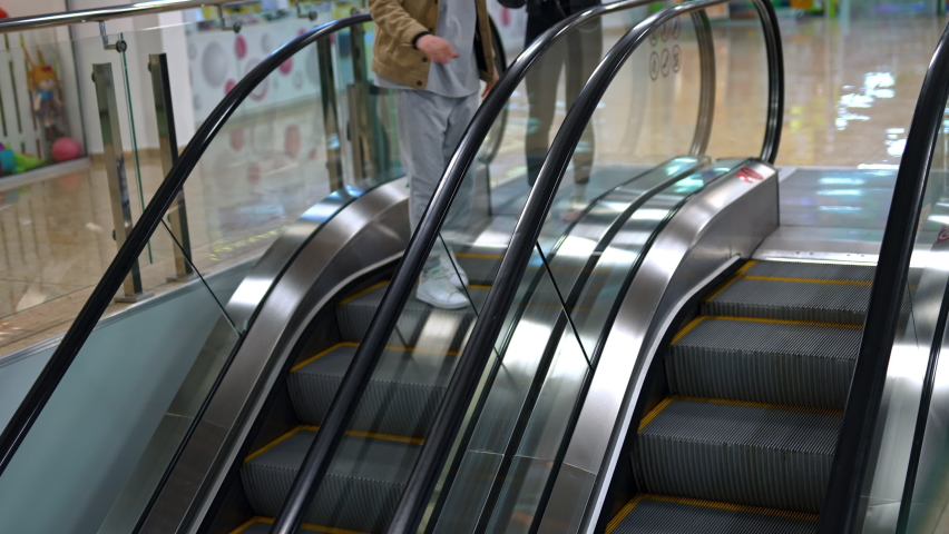 Young happy couple go down standing on escalator in the big shopping mall. People are joking and laughing cheerfully. Top view.