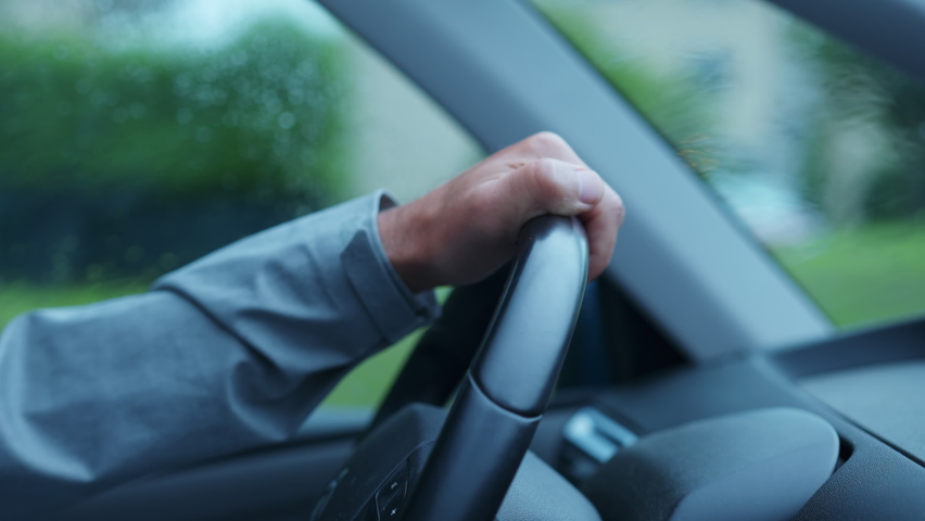 Person making a left turn with steering wheel while raining. Closeup male hands driving on road during rainy day Royalty-Free Stock Footage #1097741421