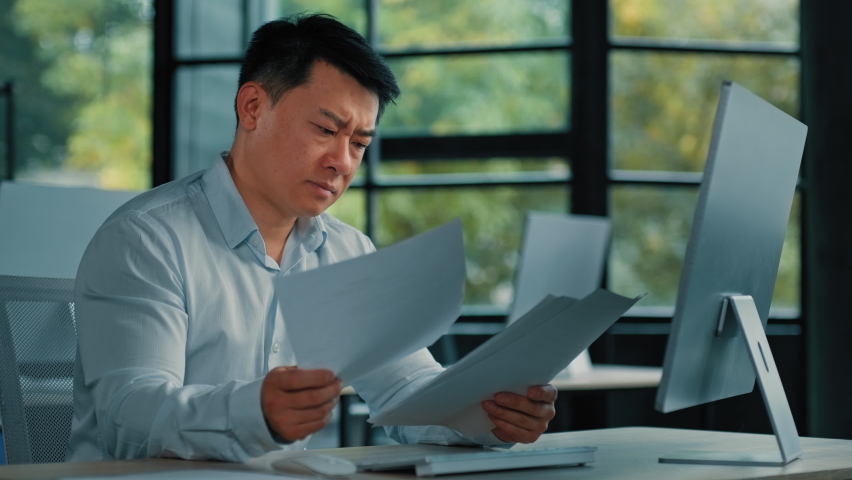 Disappointed angry Asian office manager mature man specialist lawyer banker work with paper documentation read legal documents check error bankruptcy problem negative incorrect result business failure | Shutterstock HD Video #1097742327