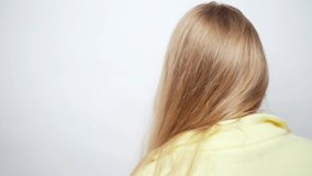 Close-up portrait young beautiful blonde woman in glasses and casual yellow sweater turns around, wave her hair, and looks at the camera with a cute charming look. White studio background stock video