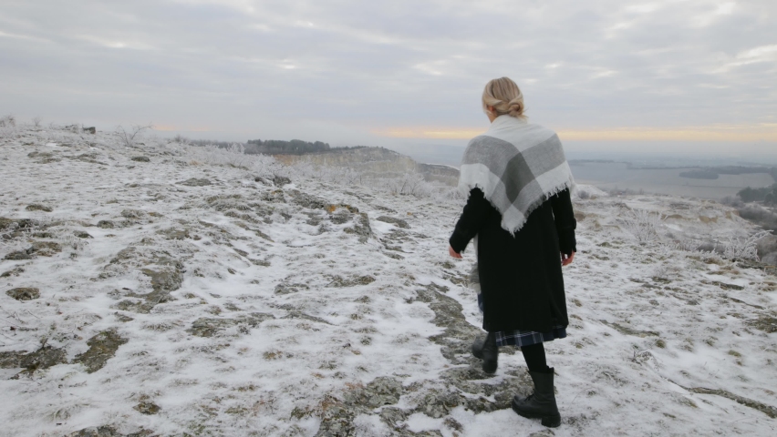 The camera follows a woman who runs alone on the hillside, approaches the edge of the cliff and stops, raises her hands up and admires the winter landscape, the atmosphere of a Christmas fairy tale