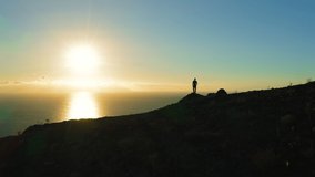 Man silhouette stands on edge of cliff and looks out at ocean during sunset. Sun touches water surface golden path in sea. Aerial drone flight. Los Gigantes Tenerife Canary Islands Spain Europe. - Powered by Shutterstock - Get 15% off with code: PIKWIZARD15