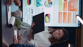 Vertical video: Employee speaking in business meeting, financial report presentation, standing near digital board with analytics charts. Team working on company research statistics, planning marketing
