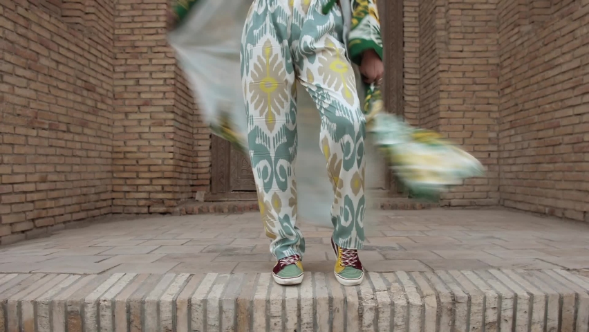4K. Overall plan. Tourism in Uzbekistan. An oriental girl in a traditional Uzbek robe dances against the backdrop of an old madrasah with a robe. Front view.	