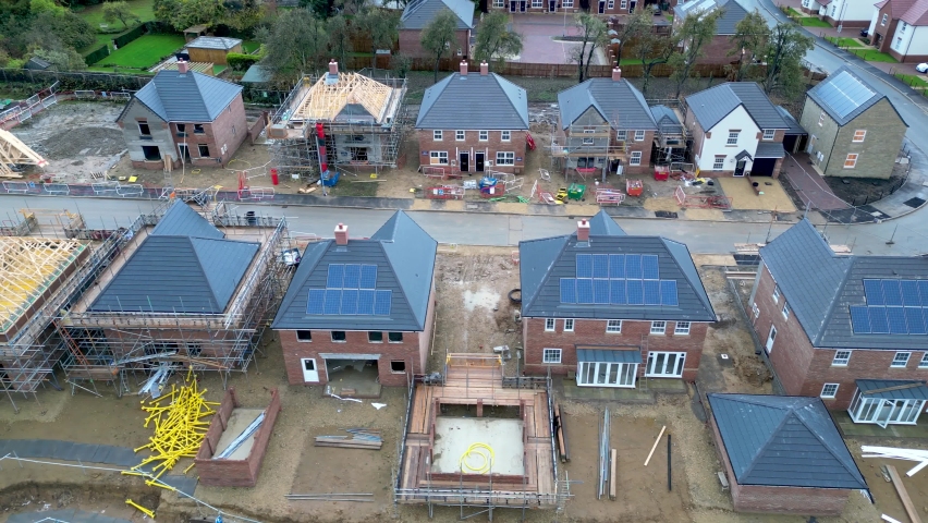 A aerial overview with a panning shot of new housing built on the construction site. Houses are fitted with solar panels on the roof. UK. Royalty-Free Stock Footage #1097755265