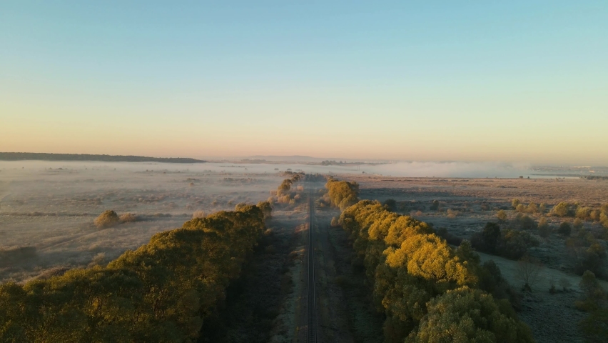 Aerial Drone footage. Copter slow move above the morning field. Beautiful view of sunrise with fog. 
The railway. Train travels concept.