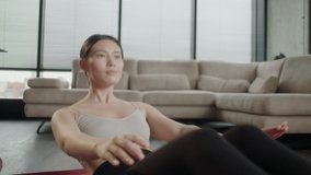 Young Sporty Asian Woman in sportswear watching online video with fitness exercises on laptop. Female fitness shakes her press on yoga mat at home. Pretty lady burning calories, practice pilates
