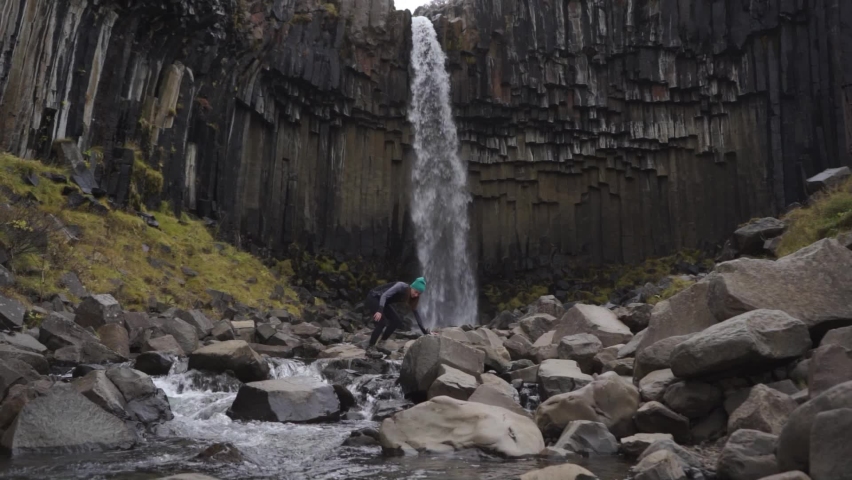 young woman tourist climbing on rocks at Svartifoss waterfall