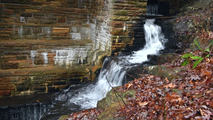 A small initial spillway on Byrd Creek Dam in Cumberland Mountain Tennessee shows the fall colors and brick details of the dam as the water flows down to the river below. Royalty-Free Stock Footage #1097769225
