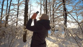 a young blond Caucasian woman while hiking in fresh air in winter forest. It takes photos on your smartphone of fabulous nature or forest. active girl smiles happy to live. Sunny frosty weather.