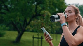 Close up of the sporty woman walking in the park after running and using smartphone. Female athlete drinking water from sport bottle, wearing smartwatch. People, sport and technology concept - Powered by Shutterstock - Get 15% off with code: PIKWIZARD15