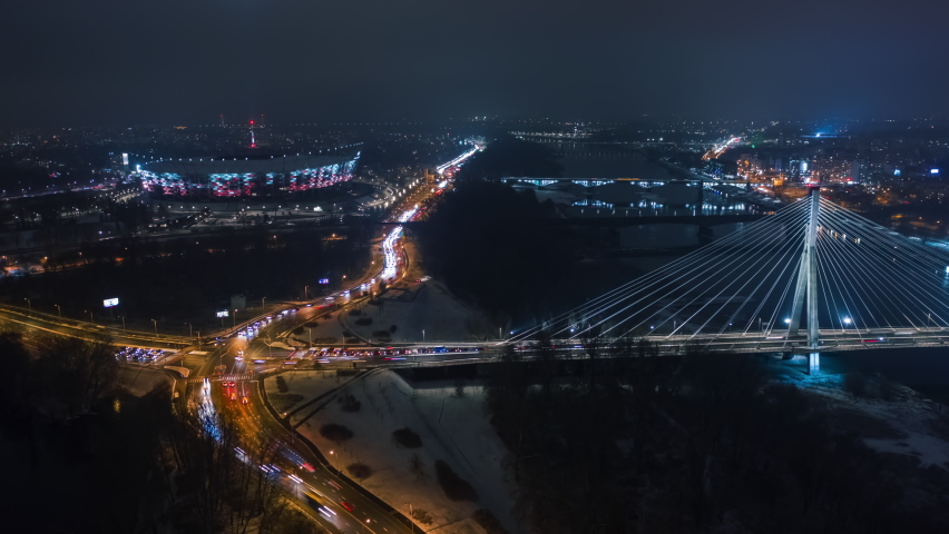 Aerial time-lapse panoramic drone shot of Warsaw city cityscape. Suspension cable bridge over Vistula river, downtown urban skyline in evening. Cinematic Warsaw panorama at night