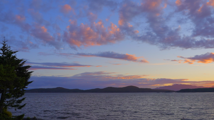 Establishing shot of ocean sunset over mountains in slow motion at summer day in Vancouver, Canada, North America. Evening time on September 2022. Still camera. ProRes 422 HQ.