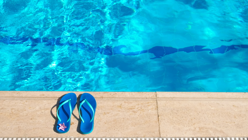 Flip flops with girl into pool. A view of blue flip-flop lay by the swimming pool under sun. A concept of swimming recreation during vacation. Royalty-Free Stock Footage #1097776251