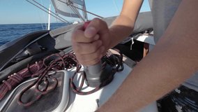Sailor's hand on a winch of sailing boat. Man pulling ropes, winding around winches.A yacht school student learns to use a yacht winch on a ship. Sailing crew tightening up main sail winding rope