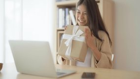 Young asian woman using computer laptop at home. Female showing gift box while on video conversation with friend. Happy birthday, Happy new year, Thanksgiving