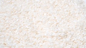 Video background of dry raw white rice on a white plate rotating on a white background. 