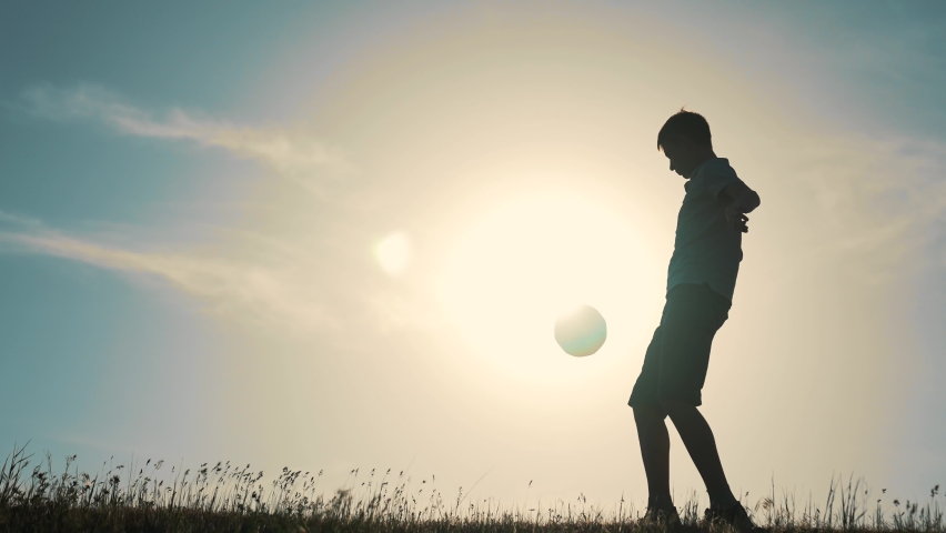 Boy juggles the ball with his foot. Silhouette of a sports child with a soccer ball. Young player kicks the ball. Active child in the park. Boy winner strives for victory. Success active happy child