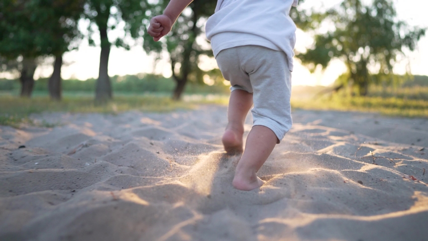 Feet running on the sand on beach. Child runs in the sun. Happy summer vacation. Child picnic in park. Bare feet of a toddler on the beach. Family vacation in nature. Cheerful kid playing in the park Royalty-Free Stock Footage #1097782281