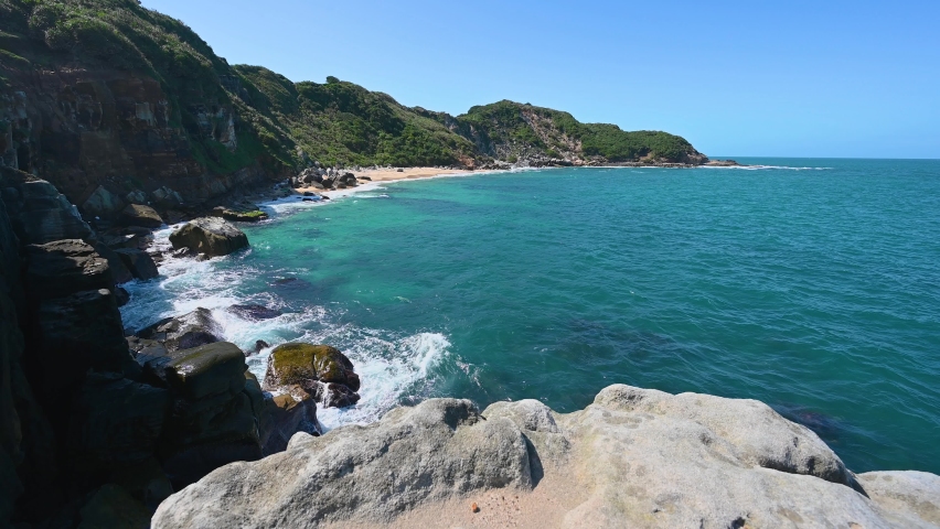 The blue water hits the rocks, producing white waves. Blue sea, rocky hills. Rocky coast, Jinshan District, New Taipei City, Taiwan.