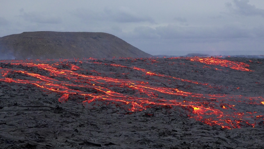 Volcanic eruption. Hot lava. Red smoke over the crater. Lava flow over volcanic earth. The lava cooling in the air while moving heavily in a great scenery and solidifying forming volcanic black rocks. - Powered by Shutterstock - Get 15% off with code: PIKWIZARD15
