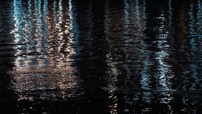 Colorful light reflects on dark rippling moving water at night. Abstract. 4K footage