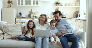 Happy family with small children sit on comfortable couch, enjoying funny on-line videos on laptop. Young parents rest with 6s kids watching movie using wireless computer together at home on weekend