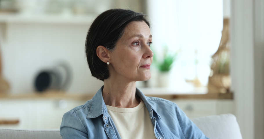 Close up head shot of attractive calm pensive middle-aged woman staring aside and thinking standing posing alone in domestic kitchen, smile looking at camera. Life on retirement, thoughts, melancholy Royalty-Free Stock Footage #1097784987