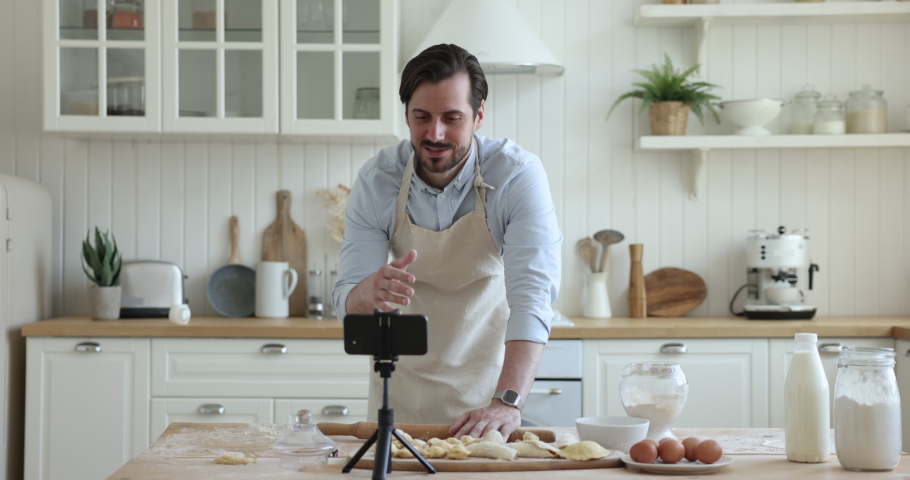 Millennial guy blogger record food class online tutorial video looks at smartphone cam and talking about pastry recipe, share cooking steps, standing in cozy kitchen at home. Vlogging, culinary, tech Royalty-Free Stock Footage #1097785059