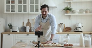 Millennial guy blogger record food class online tutorial video looks at smartphone cam and talking about pastry recipe, share cooking steps, standing in cozy kitchen at home. Vlogging, culinary, tech