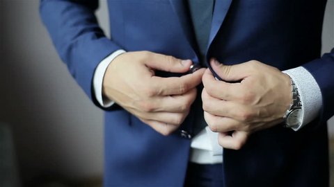 Buttoning a jacket. Stylish man in a suit fastening buttons on his jacket preparing to go out. Close up