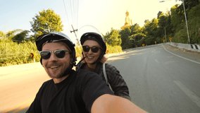 Young Mixed Raced Tourist Couple Riding Motorbike in Asia and Taking Funny Selfie Videos Using Action Camera High Quality 4K Slowmotion Footage. Thailand.