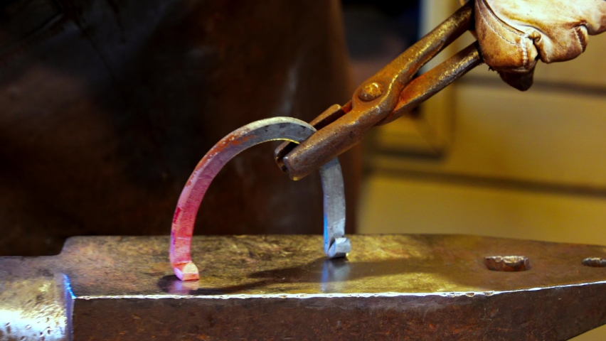 Vintage blacksmith uses tools to forge a red-hot steel billet horseshoe. A professional blacksmith works with hot metal on a blacksmith hammer. Strong man doing hard manual labor Royalty-Free Stock Footage #1097795057