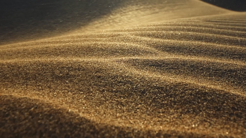 Sand storm in desert. Macro shot of sand particles blown away by the wind. Camera moves along surface of sand dune in the desert in the rays of the setting sun. Sand waving in the wind. Slow motion