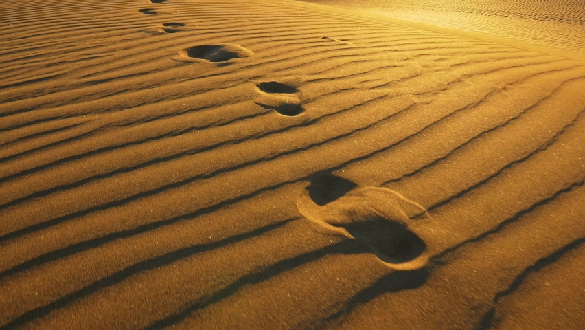 Camera follows footprints in big sand dune. Footprints in the sand in desert at warm sunset lights. UHD, 4K Royalty-Free Stock Footage #1097799235