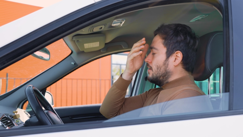 A young man guy sits in a car holding his hand on his head which hurts. The driver behind the wheel stopped to catch his breath. He probably has a headache. Royalty-Free Stock Footage #1097804919