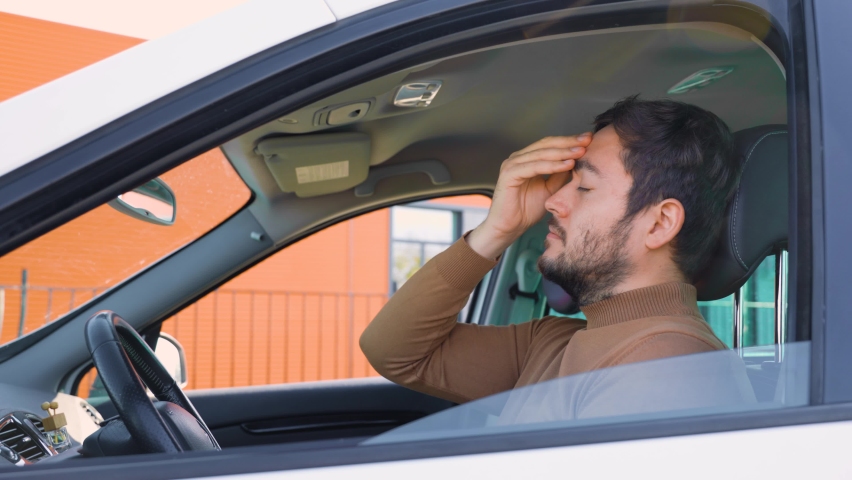 A young man guy sits in a car holding his hand on his head which hurts. The driver behind the wheel stopped to catch his breath. He probably has a headache. | Shutterstock HD Video #1097804919