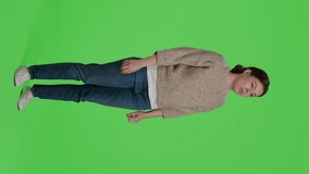 Vertical video: Side view of tired girl yawning in studio, posing over green screen background. Young adult being exhausted and sleepy standing over isolated full body greenscreen backdrop, falling