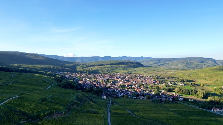Panoramic aerial drone top view of the rural village of Orschwihr (Upper-Rhine, Alsace, France) in summer day, between vineyards and Vosges mountains, with houses, right travelling movement Royalty-Free Stock Footage #1097814403