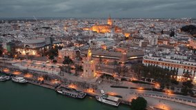 Seville old town with Torre del Oro tower, Cathedral and other historic buildings at night, Andalusia region, Spain. Aerial drone footage of Seville cityscape at night with street Illumination.