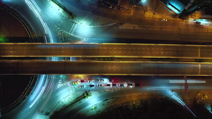 Time-lapse of car traffic transportation on road at junction intersection, 4K. Aerial view of road interchange or highway intersection with busy urban traffic speeding on the road at night. Royalty-Free Stock Footage #1097817963