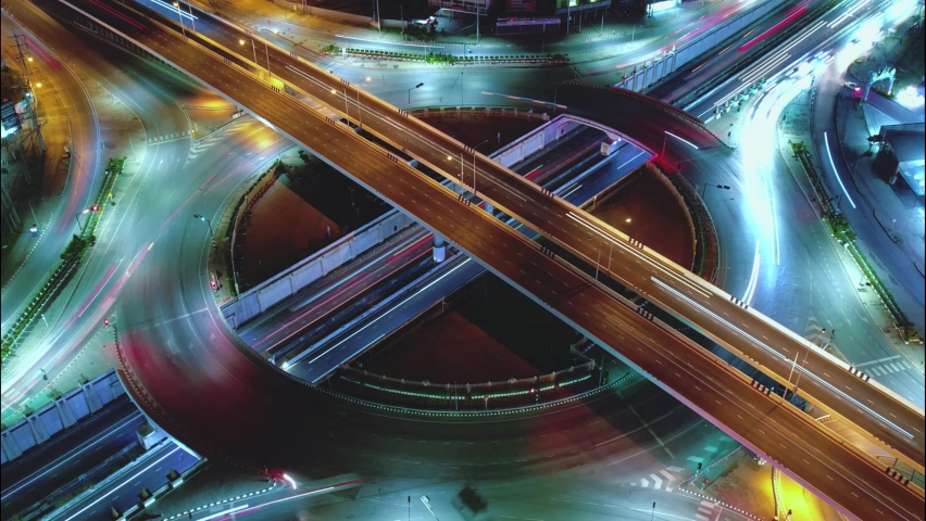 Time-lapse of car traffic transportation on road at junction intersection, 4K. Aerial view of road interchange or highway intersection with busy urban traffic speeding on the road at night. Royalty-Free Stock Footage #1097817981