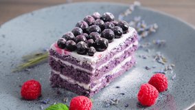 A piece of purple velvet cake with cream sprinkled with sugar served on plate decorated with lavender, blueberry and raspberry rotating, slow motion rotation video clip, 4k close up footage