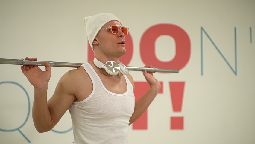 a man in a white hat and white t-shirt squats in the fitness room. FullHD high quality video. slow motion video