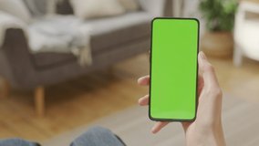 Handheld Camera: Point of View of Woman on Living Room Holding Chroma Key Green Screen Smartphone Watching Content Without Touching or Swiping. Girl Using Mobile Phone, Browsing Internet, Watching