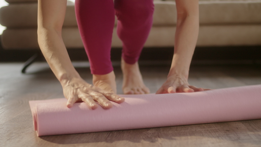 Middle age female with yoga mat at home. Attractive young woman unfolding red yoga or fitness mat before working out at home in living room. Healthy life, keep fit concepts.