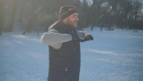Adult man is exercising in park in winter. He is stretching his body and warming up for jogging. 4K video.