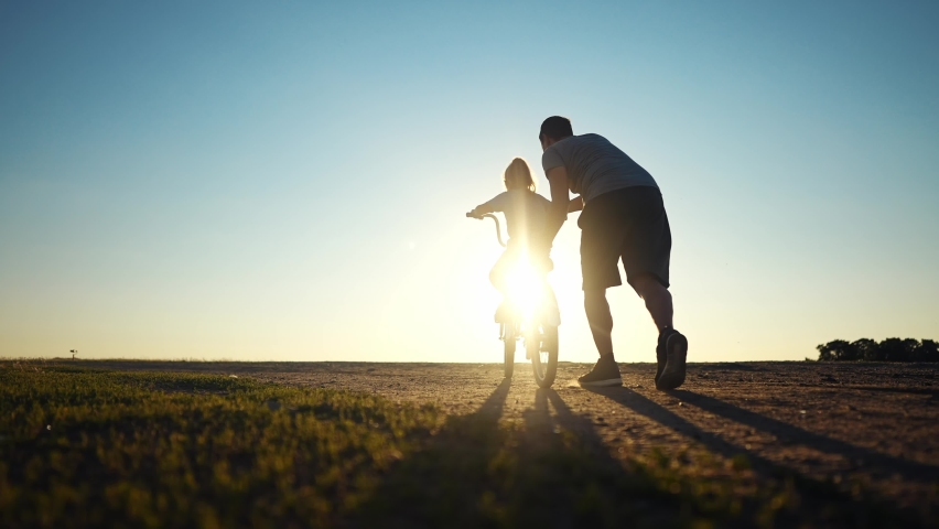 dad teaches daughter to ride a bike. happy family childhood dream concept. father and little daughter learn to ride a bike silhouette in the park. happy family goes in for sports outdoors sunlight Royalty-Free Stock Footage #1097828465
