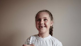 little girl smiling holding a glass of water. the child looks close-up into the video camera. happy family childhood dream concept. lifestyle portrait girl daughter smiling funny indoors